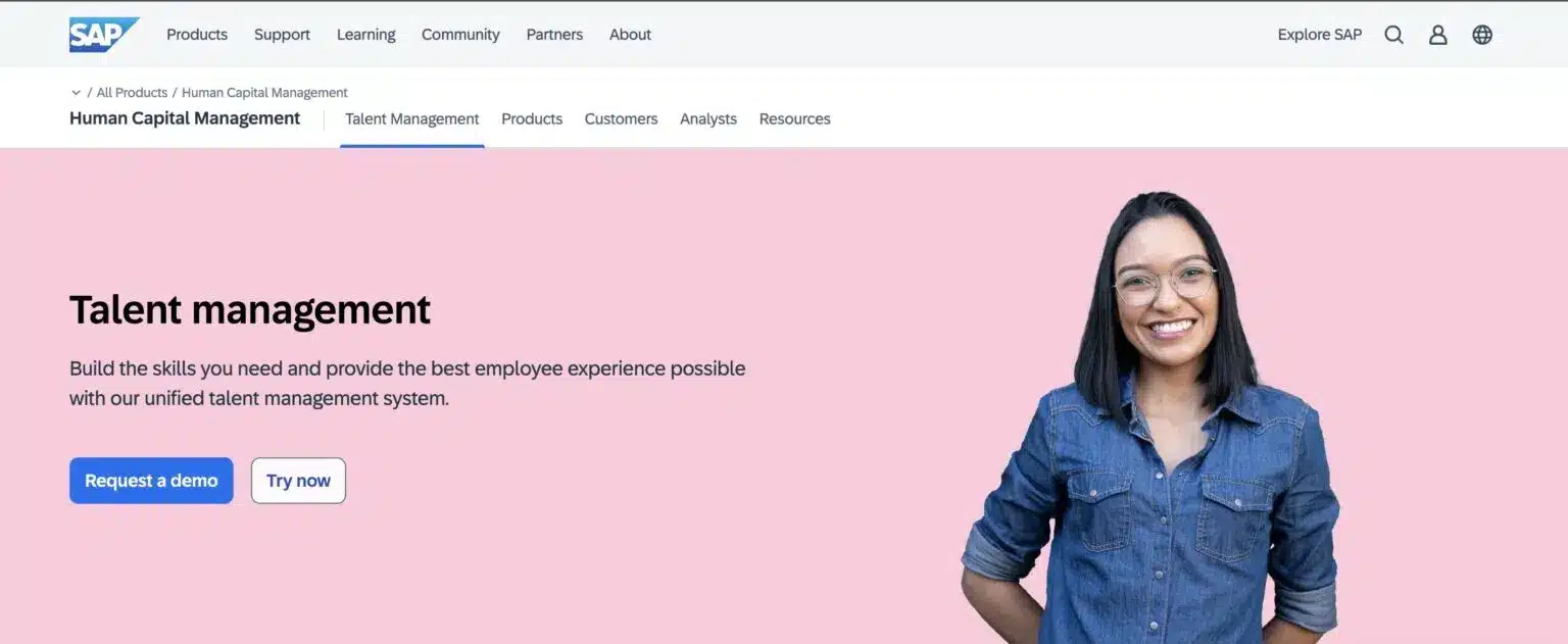 SAP Talent Management webpage with the headline "Talent management" and a description of their unified talent management system. A button to "Request a demo" and another to "Try now" are visible. On the right, a smiling woman with dark hair and glasses, possibly of South Asian descent, is shown against a light pink background. Navigation links for SAP products, support, learning, community, partners, and about are at the top.